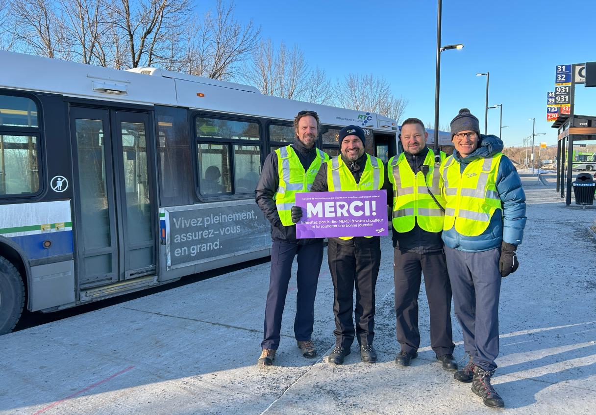 Des employés du RTC tiennent une affiche de remerciement devant un autobus